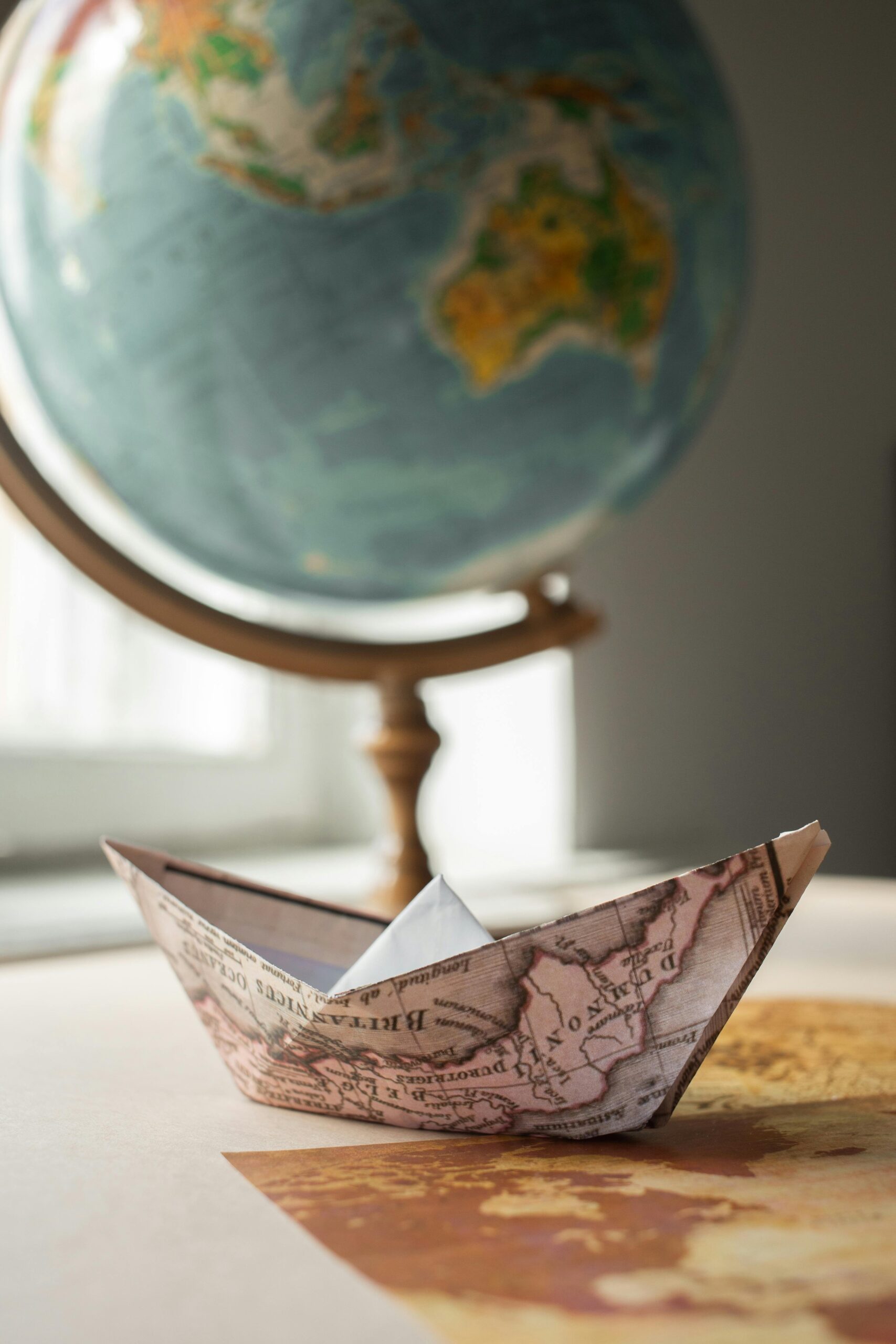 An origami boat made from a map rests near a globe, symbolizing global travel and exploration.